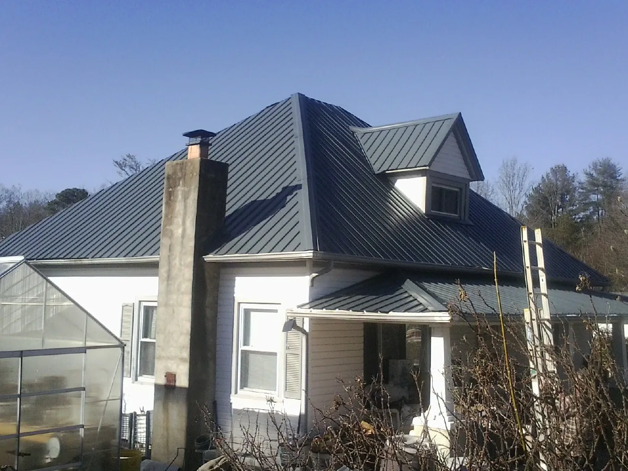 Dark blue standing seam metal roof on a white farmhouse with dormer — Slate & Tile Roof Repair by Roofing Brothers in Schneider