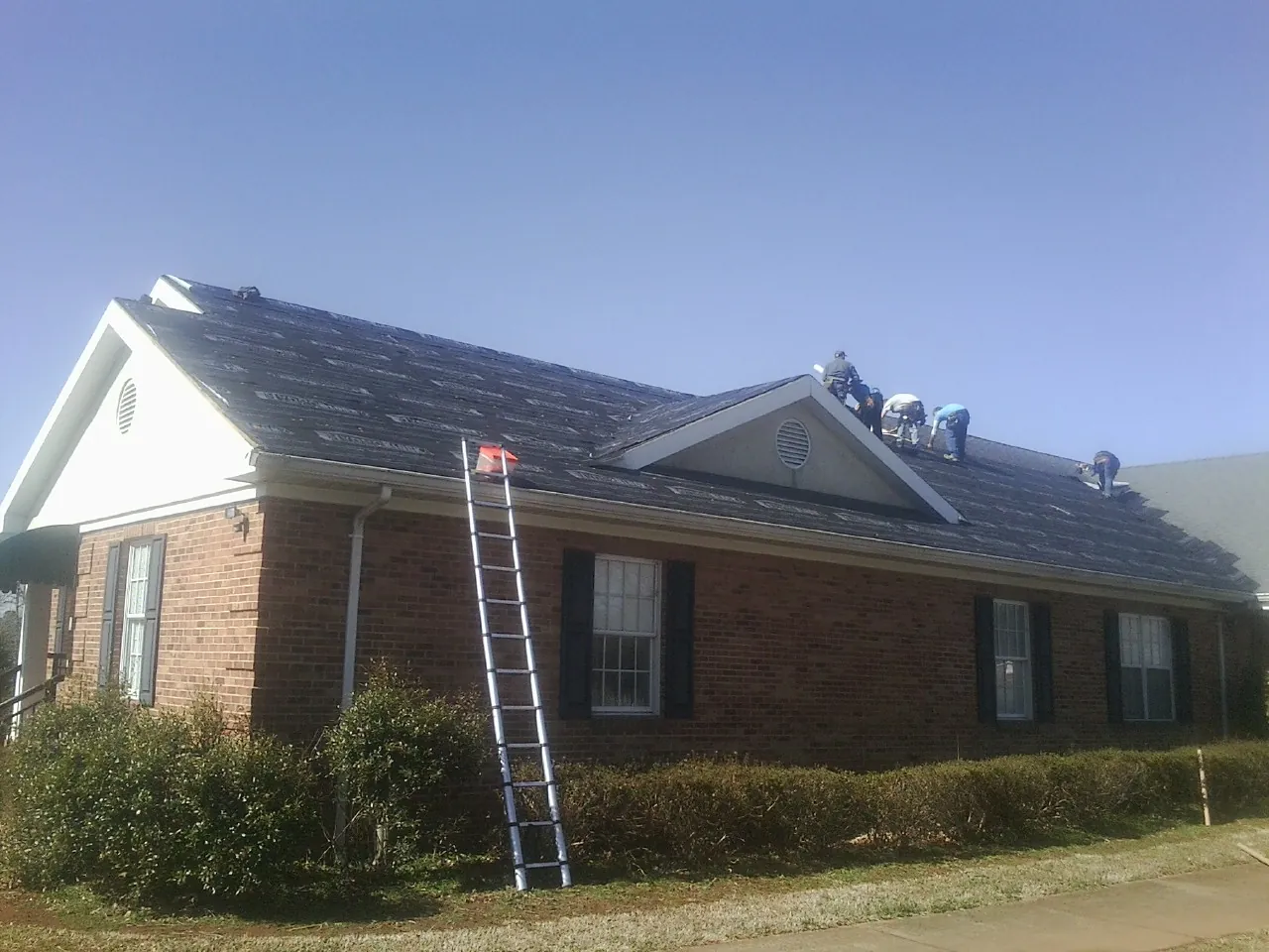 Crew tearing shingles off a brick ranch roof with a ladder set — Emergency Roof Repair work by our crew in Schneider