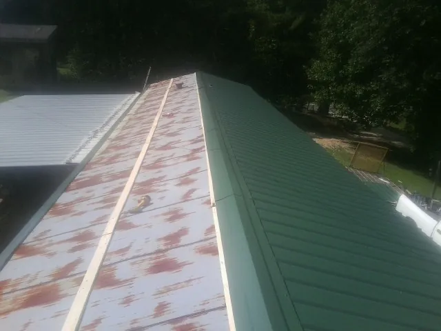 Old rusted panels beside newly installed green metal roofing — Wind Damage Roof Repair by Roofing Brothers in Schneider