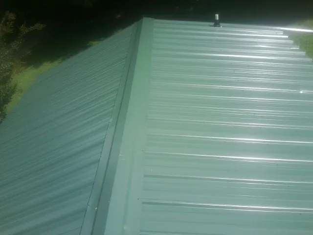 New green metal panels meeting at the ridge of a roof — Flat Roof Repair work by our crew in Schneider