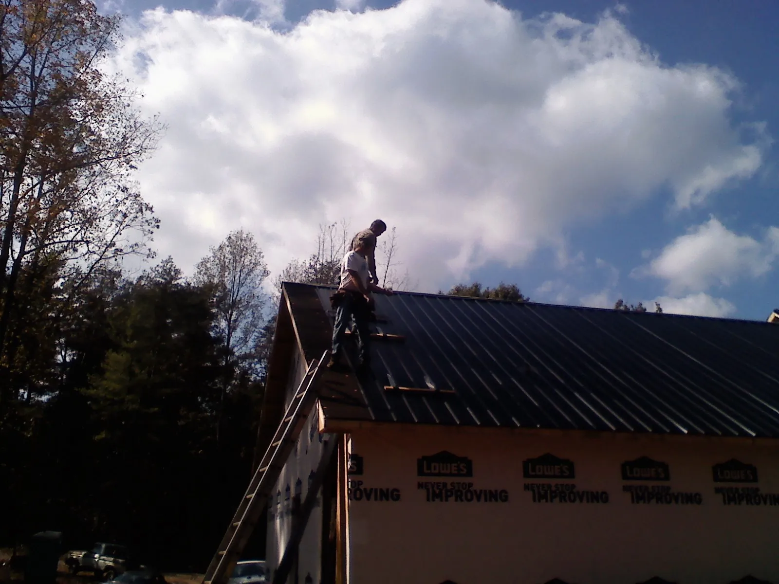 Roofer fastening dark metal panels high against a cloudy sky, from a Roof Inspection job in Schneider