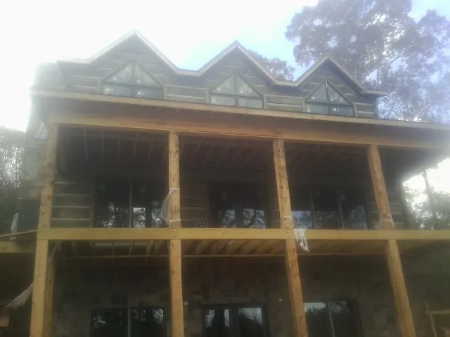 Dormers and porch framing on a large log home under construction — Roof Coating work by our crew in Schneider