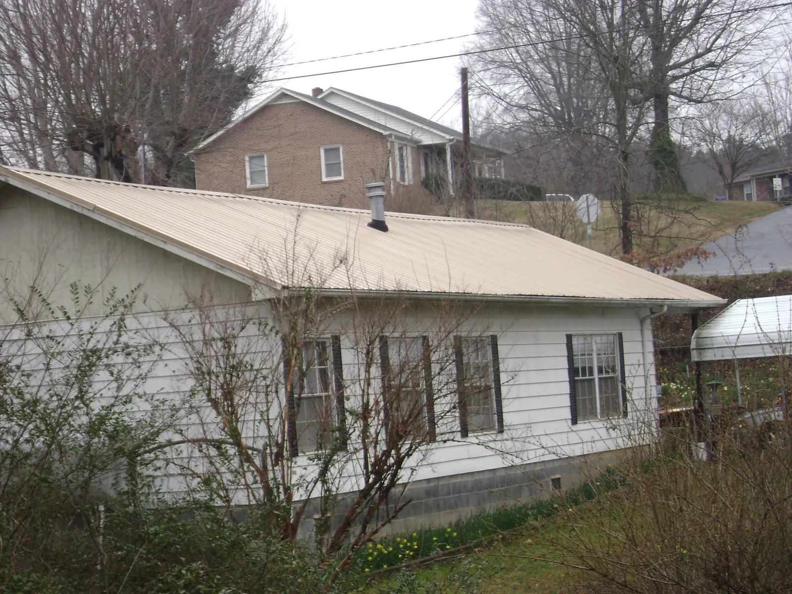 Tan metal roof on a white sided house set into a hillside — Commercial Roofing by Roofing Brothers in Schneider